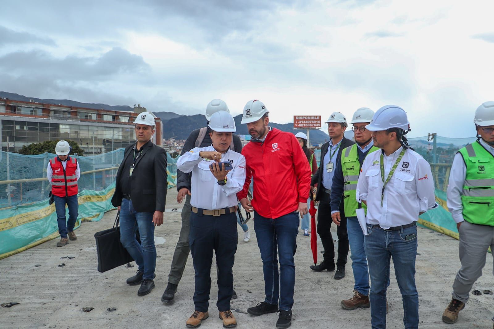 El director del IDU le muestra al alcalde, Carlos Fernando Galán, en su celular los avances en la construcción del puente. A su alrededor los caocmpañas varias personas de alcaldía e IDU